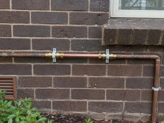 Repaired copper water pipe on a brick exterior wall under a window in Haberfield