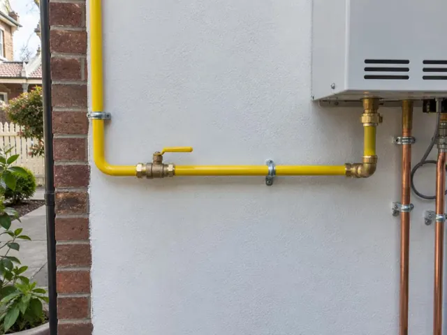 Yellow gas pipe and fittings on an exterior white wall beside a brick corner in Balmain