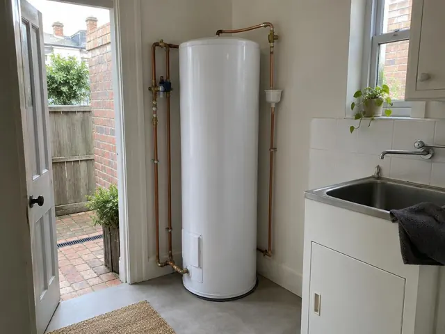 White hot water tank beside a laundry sink and tiled wall in a home utility area in Rozelle